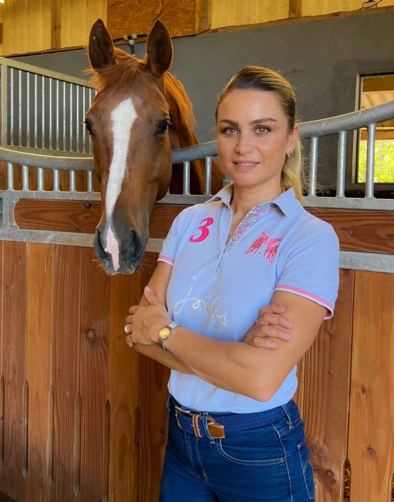 Femme et cheval bai dans une écurie en polo Jolie femme souriante à côté de la tête d'un cheval bai avec liste blanche dans une écurie; polo Joules '3'.