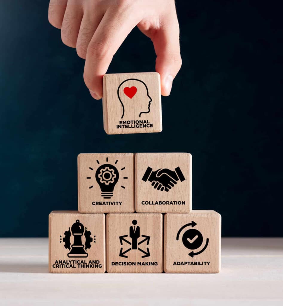 Main plaçant un bloc « Emotional Intelligence » au-dessus de cinq autres blocs représentant Créativité, Collaboration, Pensée Critique, Prise de Décision et Adaptabilité.